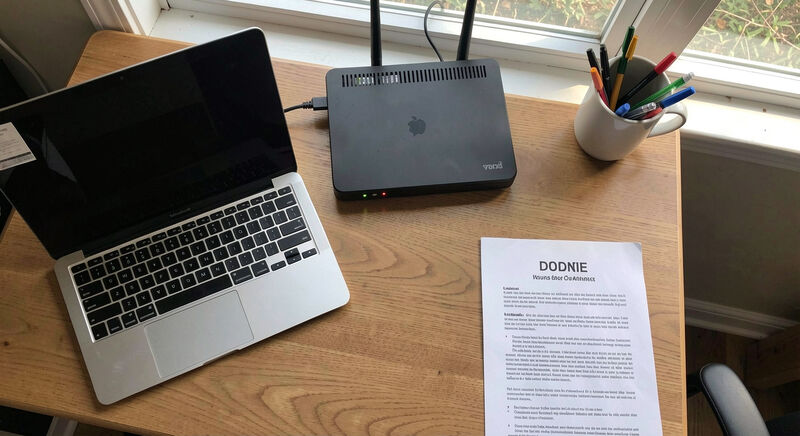 A small church office desk with a laptop, a network router and a mug of pens.